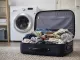 Geöffneter Koffer mit Urlaubswäsche vor einer Waschmaschine
