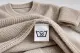 Beiger Strickpullover mit Pflegeetikett, auf dem das Waschsymbol Bottich mit 30 zu sehen ist